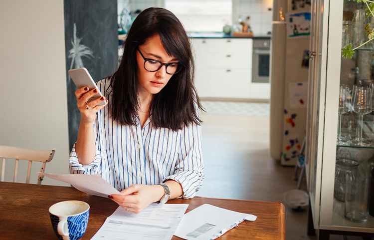 A woman in her 20s looks at a bill while holding her phone